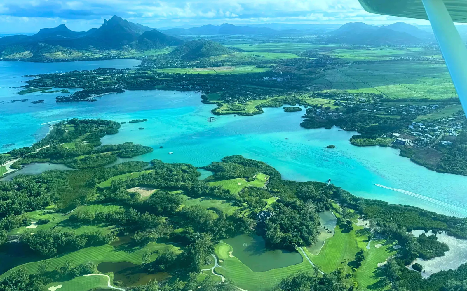 Вид с гидросамолёта на восточную лагуну Маврикия: зелёные островки, поля для гольфа, прибрежные поселения и горы вдали.